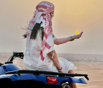 A visitor sitting on a blue quad bike in the dunes at sunset