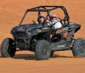 Two visitors riding a black Polaris buggy across the dunes