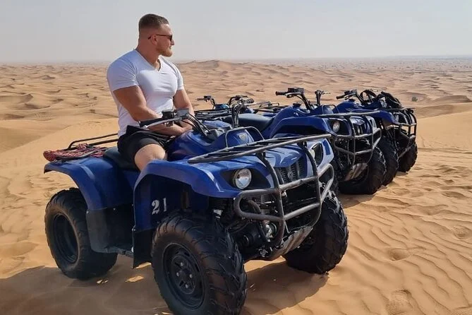 A visitor sitting beside a row of blue quad bikes in the desert